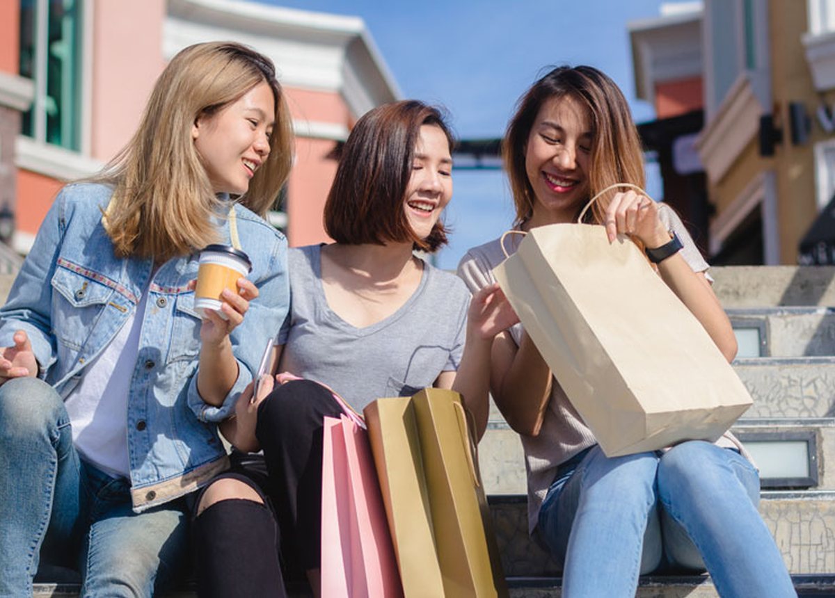 Three friends sitting on steps with shopping bags