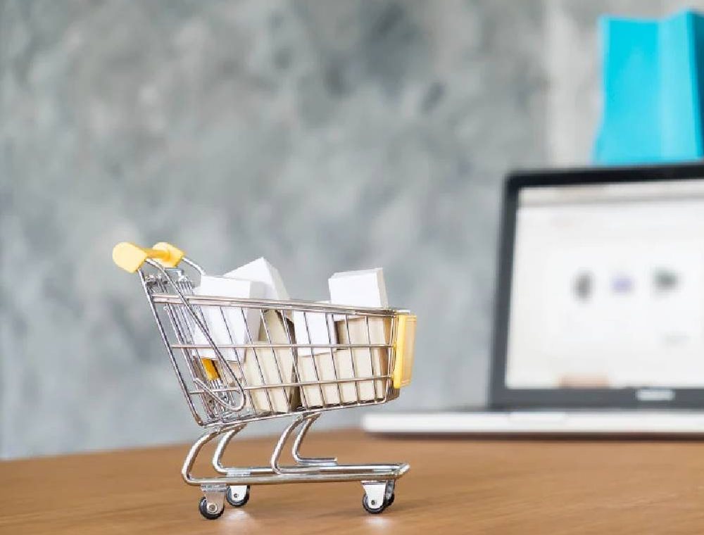 A tiny shopping cart next to a laptop